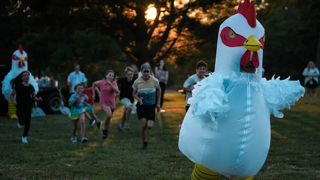 Kids racing an inflatable chicken across the field at sunset